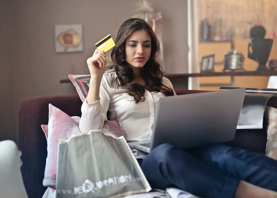 Young Adult woman using her credit card to shop online while holding laptop on her lap