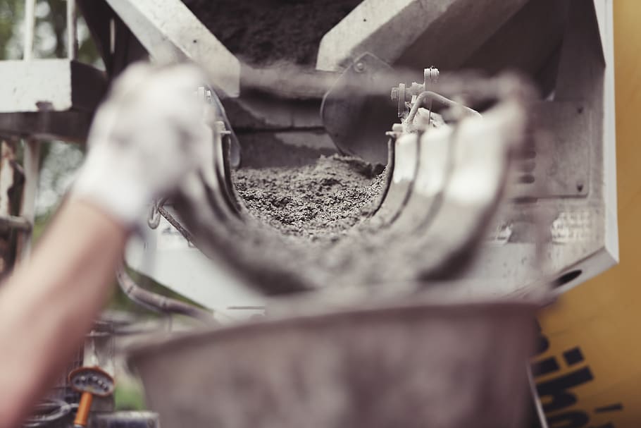 This picture shows the scene of a construction site. In the foreground a hand wearing work gloves is carrying a bucket. In the background a cement truck is visible. Cement is flowing from the truck into the bucket., HD wallpaper