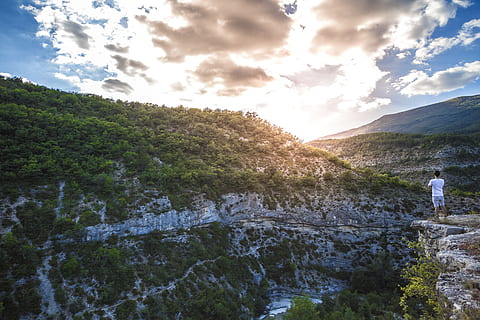 Man in White Shirt Standing on Top of Mountain Cliff Under Cumulus Clouds HD wallpaper