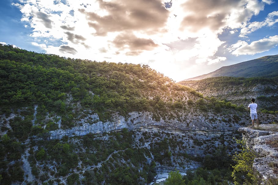 Man in White Shirt Standing on Top of Mountain Cliff Under Cumulus Clouds HD wallpaper
