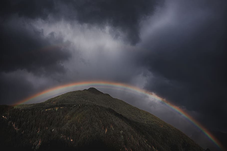low angle photo of mountain under rainbow and cloudy sky at daytime HD wallpaper