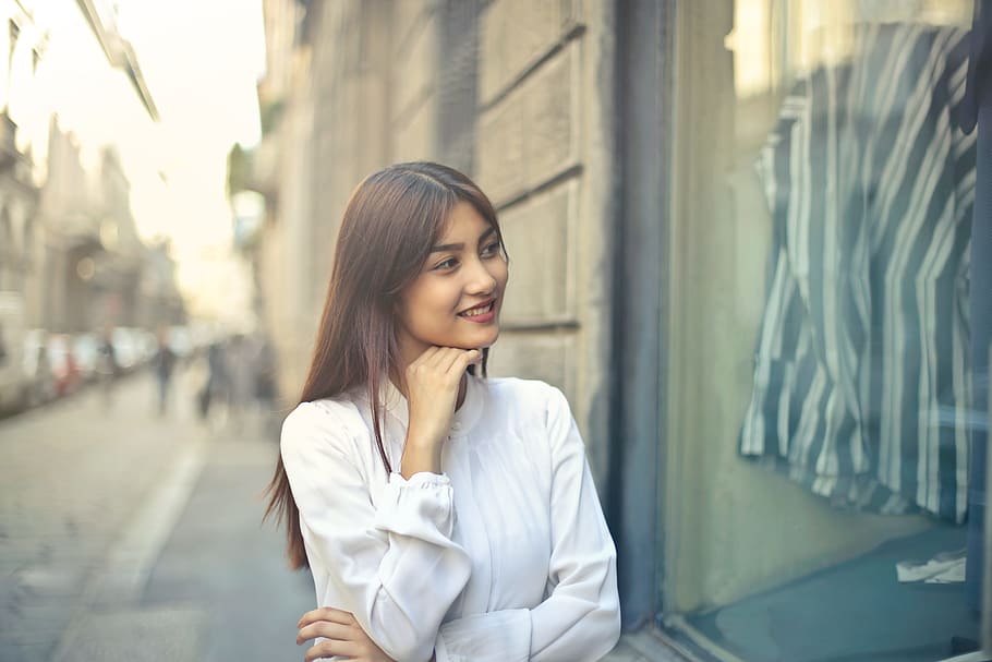 Young Asian Woman In White Shirt With Hand On Chin Doing Window Shopping On The Street