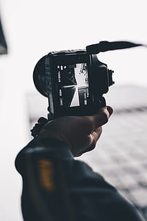 person taking low-angle photo of high-rise buildings using black DSLR camera during daytime HD wallpaper