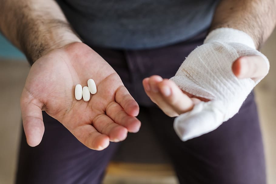 Man Holding Three White Medication Pills, arms, bandage, close-up
