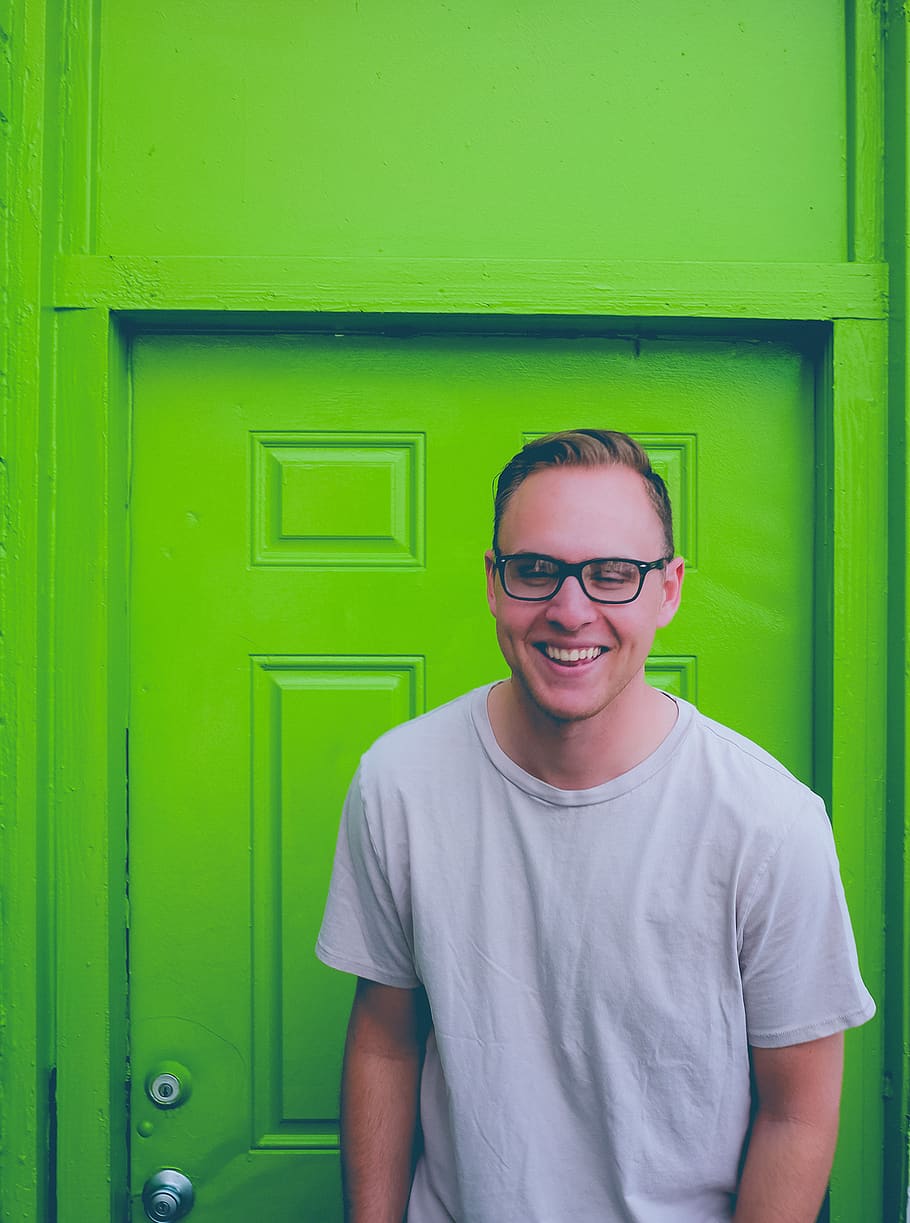 A man wearing glasses, smiling while standing in front of a green door.