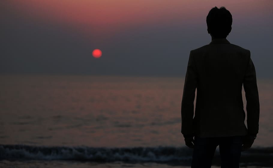 Silhouette Photo of a Man Standing in Front of the Body of Water during Sunset HD wallpaper