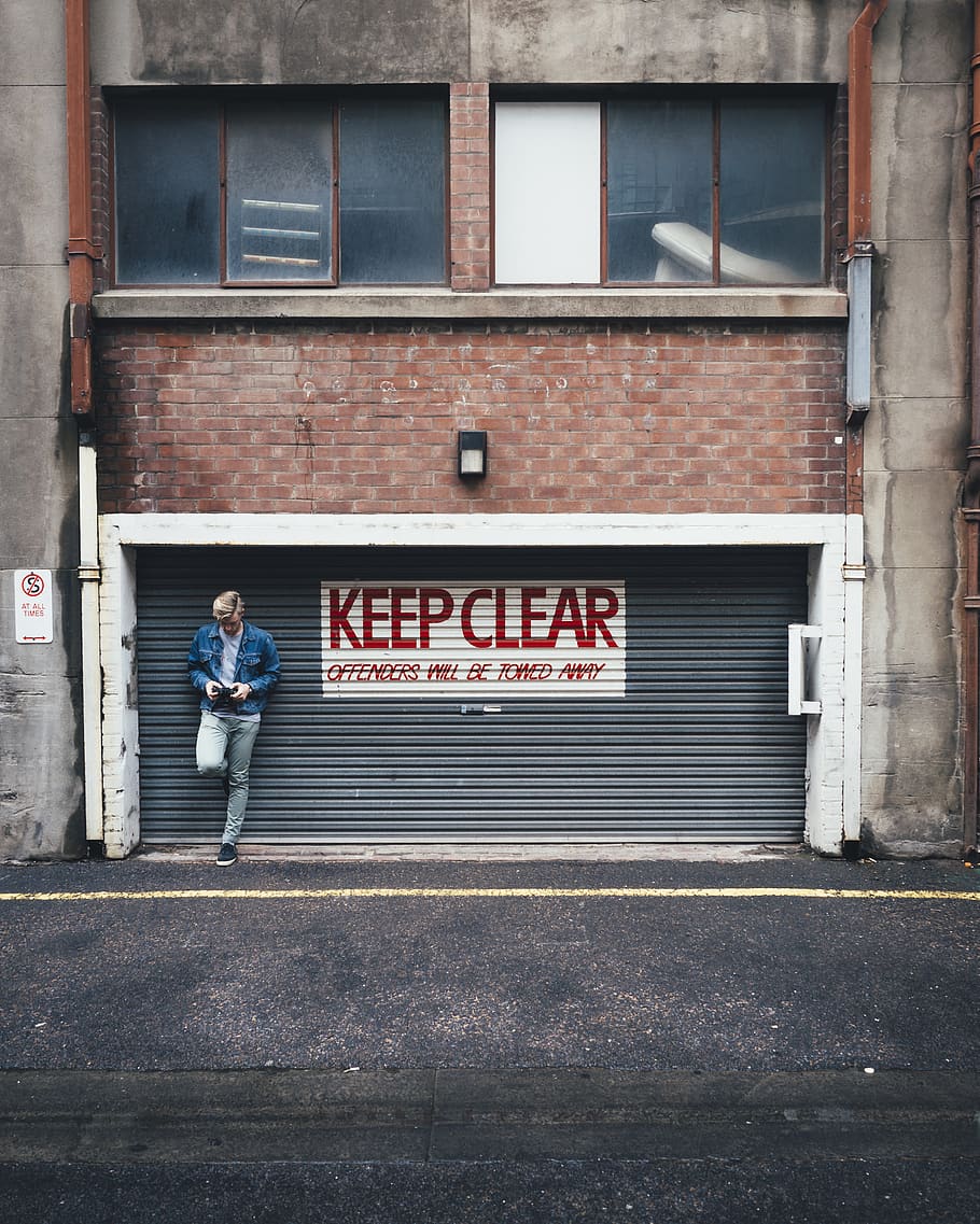 man wearing blue denim jacket while leaning against roller shutter HD wallpaper