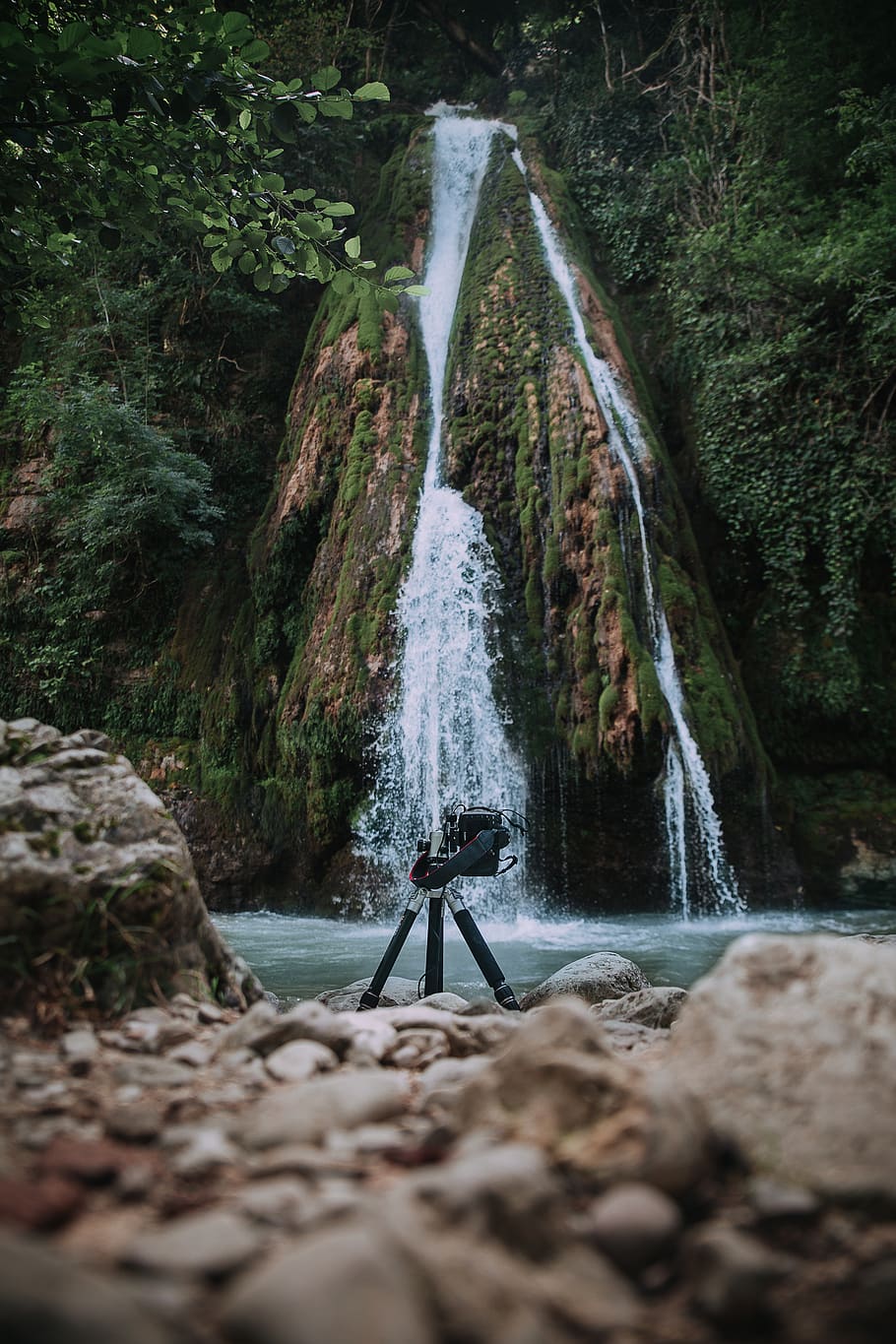 tripod on rocky shore with waterfall background, river, nature