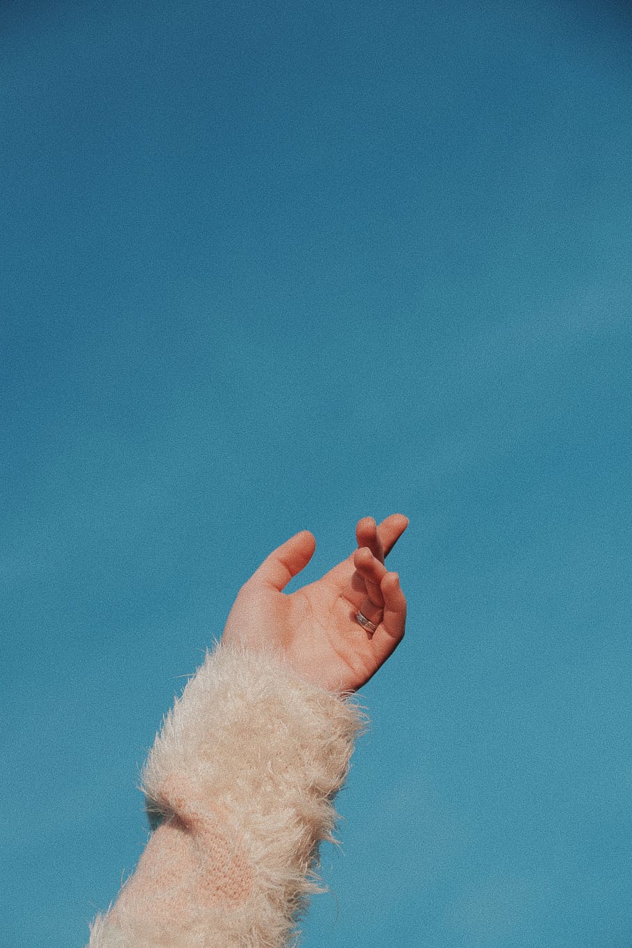 human hand wearing beige fur sleeved under blue sky, finger, person