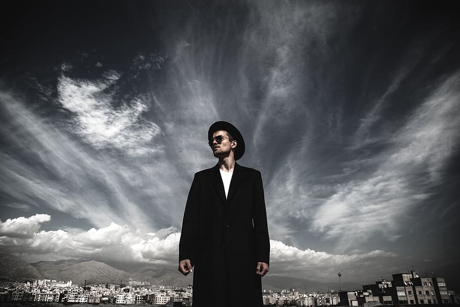 man wearing black coat and hat standing below cloudy day, clothing