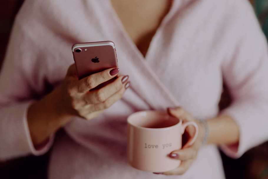 A woman in a pink sweater holds a pink iPhone and a pink cup in her hands