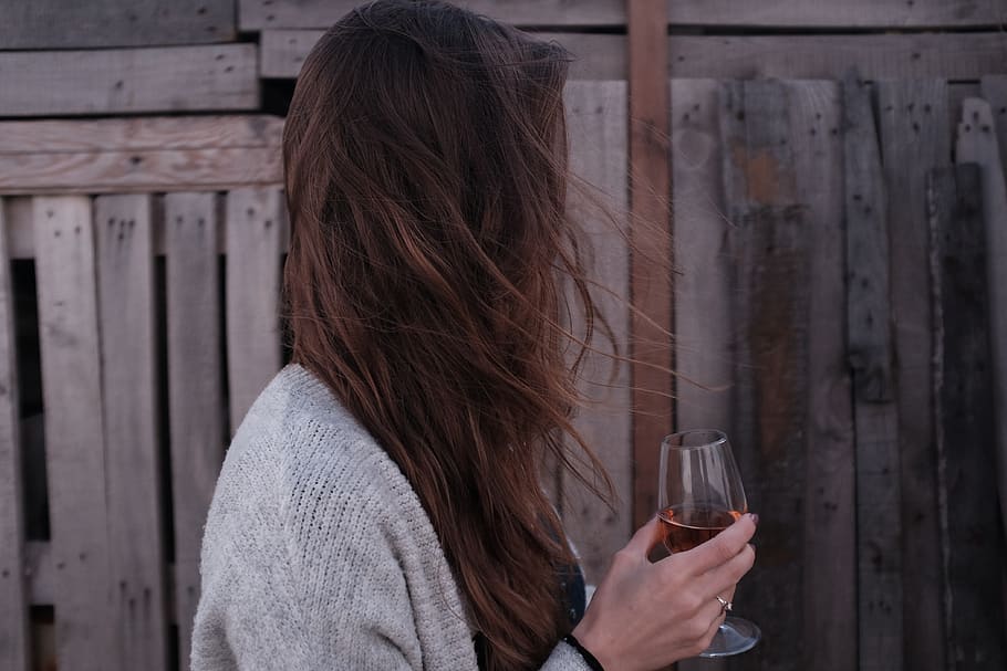 woman holding wine glass standing in front of wooden fence, human