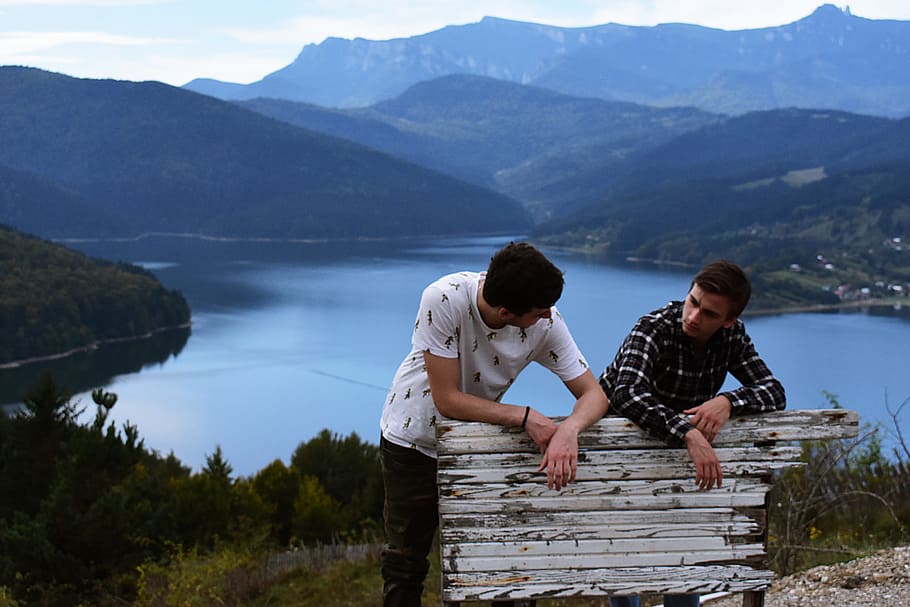 Two Person Standing at the Back of White Wooden Board Near the Body of Water HD wallpaper