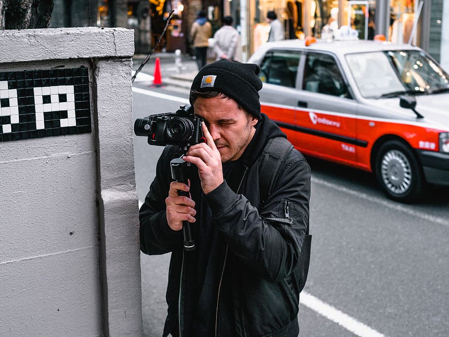 Man Holding Camera, beanie, bonnet, car, city, depth of field, HD wallpaper