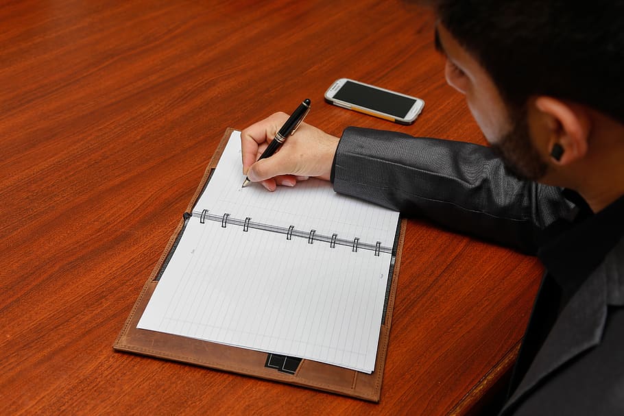 Man Writing on Notebook, desk, pen, person, one person, paper HD wallpaper