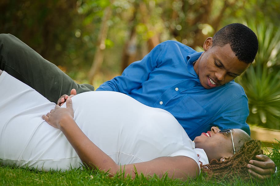 Pregnant Woman Lying Beside Man in Grass Ground, baby belly, baby bump