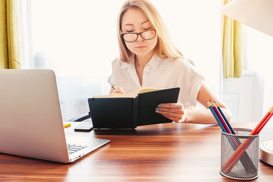 Young woman make notes in her diary. Laptop and pencils on a table in front of her HD wallpaper