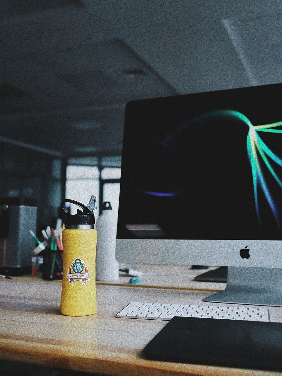 powered on silver iMac beside yellow tumbler, desktop, dark office