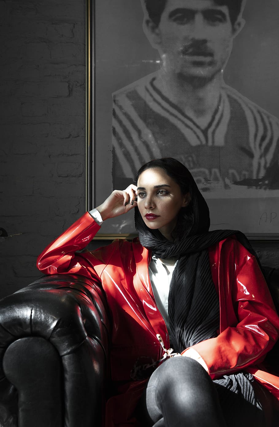 woman sitting on black sofa behind portriat on wall, apparel