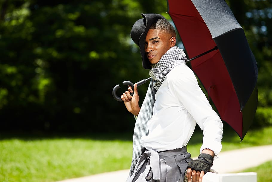 man wearing black hat holding black umbrella by the pathway, apparel