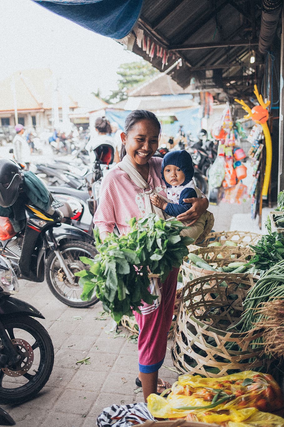 Smiling Woman Carrying Baby and Holding Green Leafy Vegetable HD wallpaper