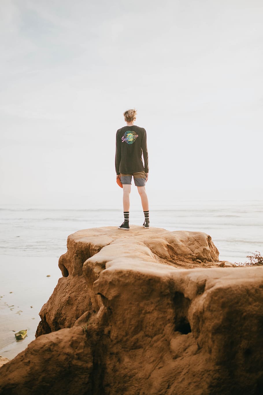person standing at the edge of a cliff in front of ocean during daytime HD wallpaper