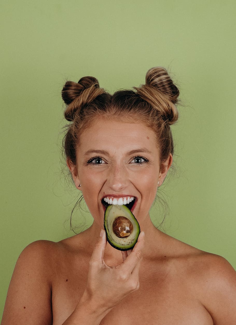 woman holding sliced avocado, teeth, face, eye, fruit, hair, earring HD wallpaper