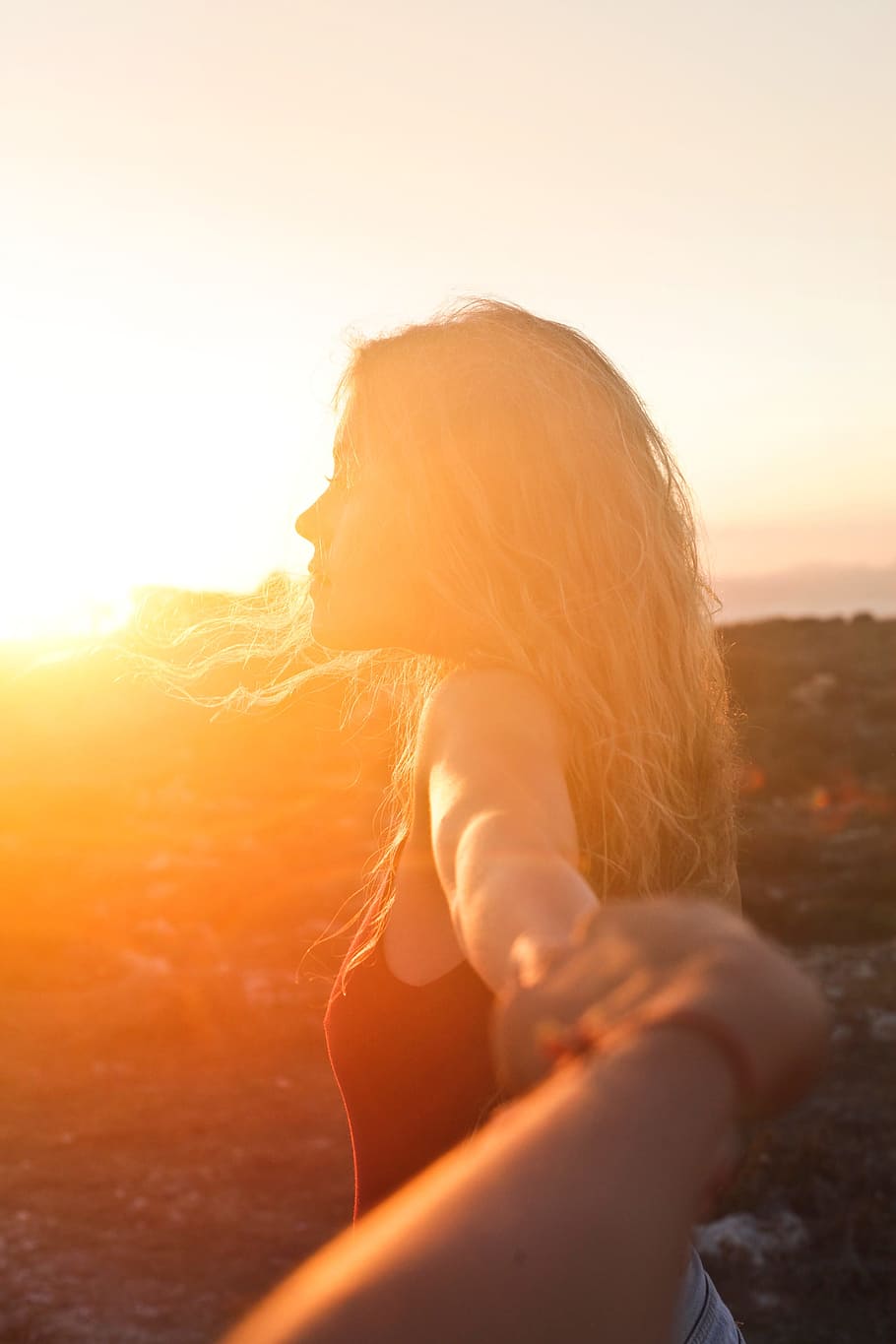 A young blonde woman looking at the sunset with her hand held by another hand