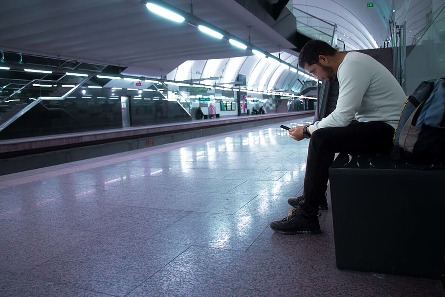 man sitting while using smartphone in train station, indoors HD wallpaper