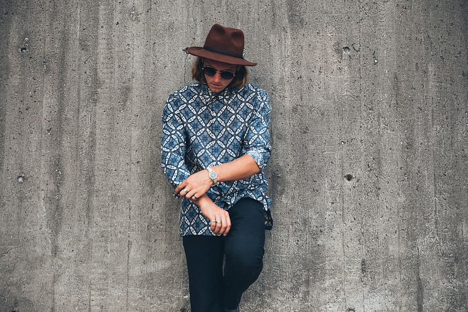 A young caucasian man wearing patterned shirt and brown hat posing outdoors
