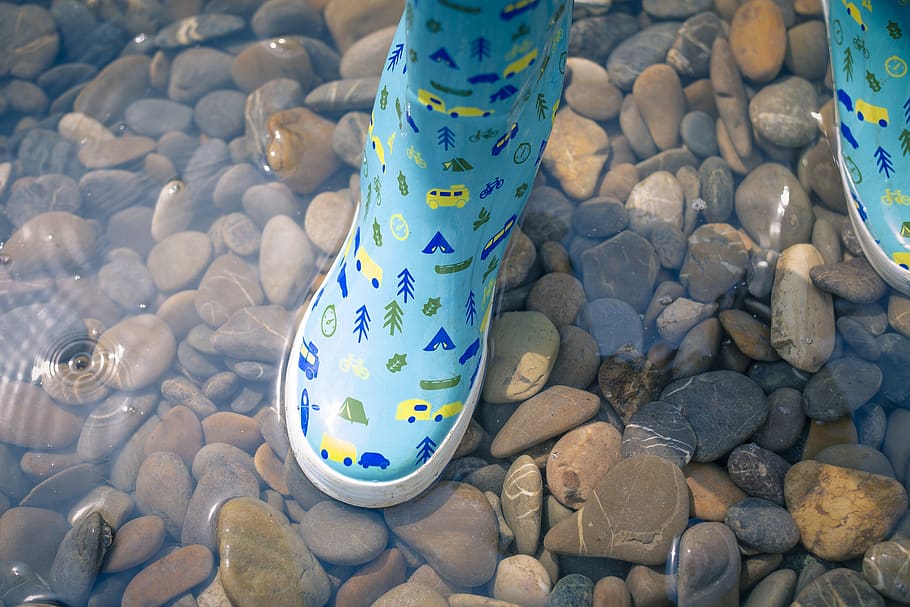 person wearing blue-green-and-yellow rain boots, solid, rock