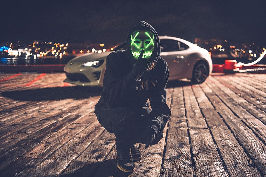 person wearing white and green mask with LED beside white coupe