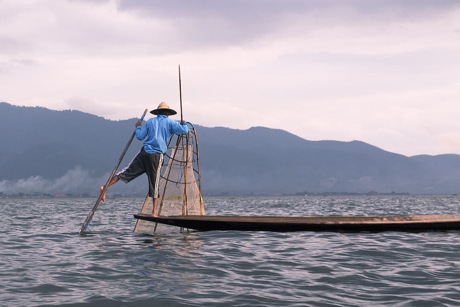 man riding boat while fishing during day time, inle lake, myanmar (burma)
