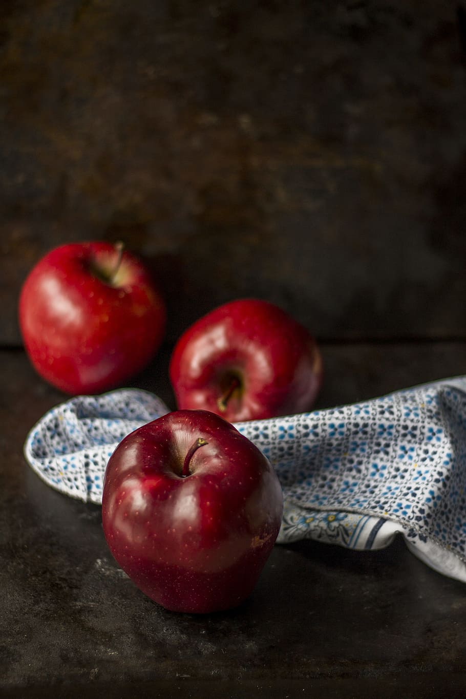 three red apples on brown surface, fruit, linen, napkin, still life