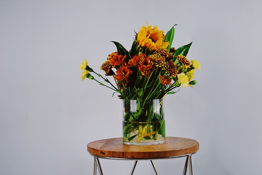 Orange, Red, and Yellow Petaled Flowers in Clear Glass Vase on Round Brown Wooden Table HD wallpaper