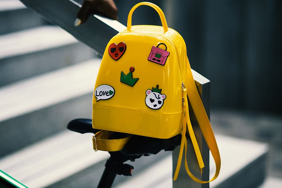 Yellow Backpack With Five Assorted Stickers on Grey Metal Stairway Rail HD wallpaper