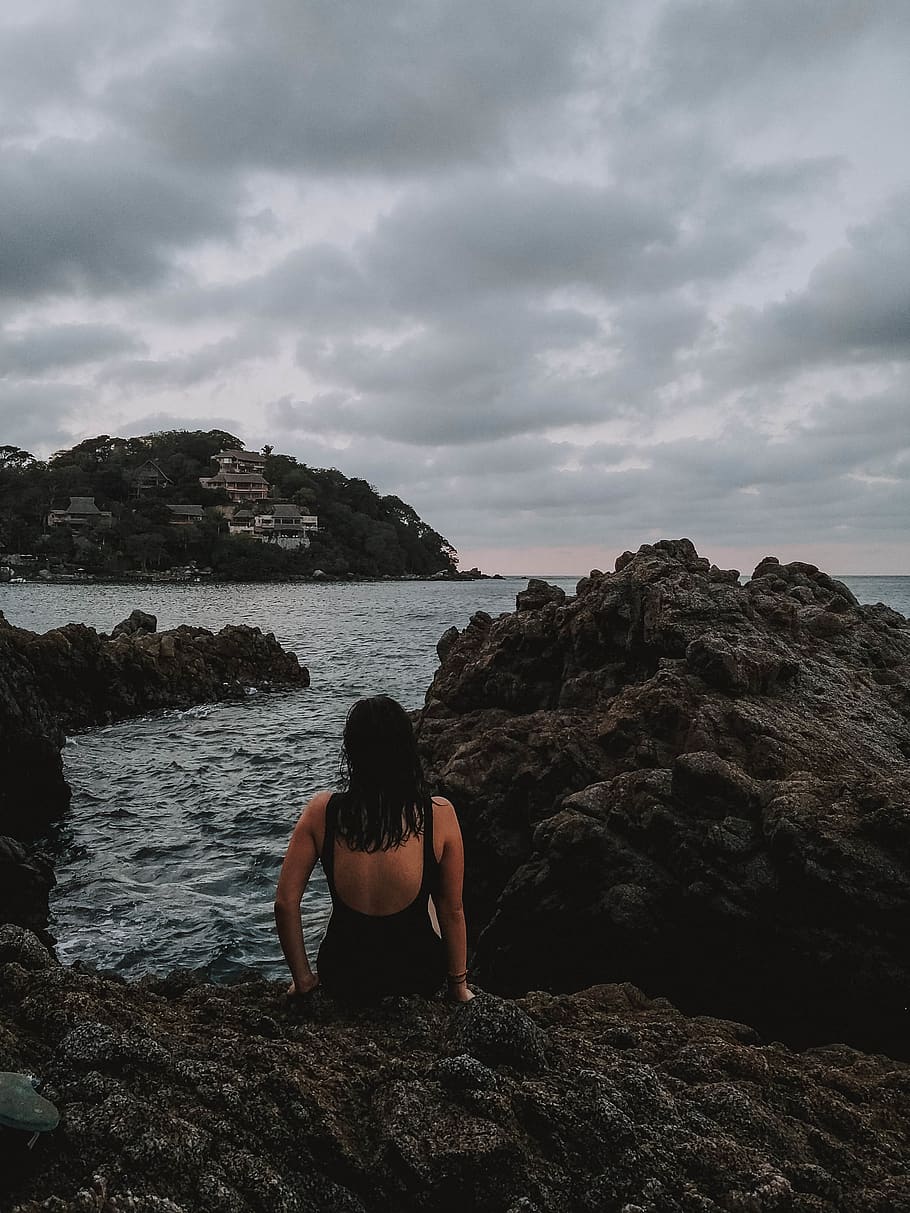 woman wearing black tank monokini sitting on rock formation near body of water during daytime, HD wallpaper