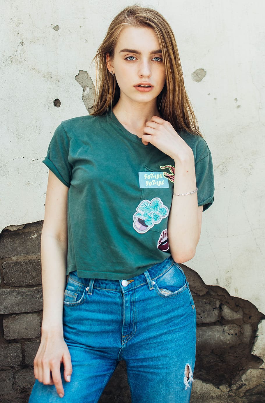 woman wearing green crew-neck t-shirt and blue jeans standing beside wall, HD wallpaper