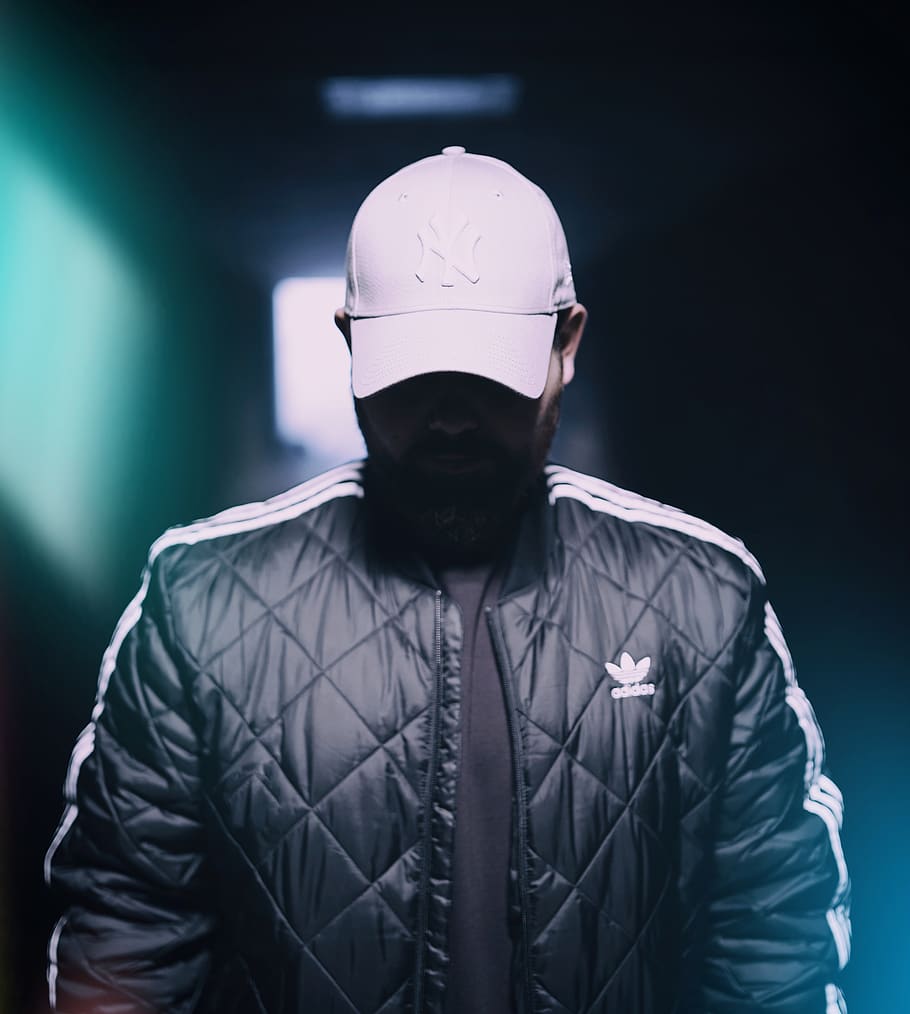 selective focus photograph of man in black adidas zip-up jacket and white New York Yankees curve-brimmed cap