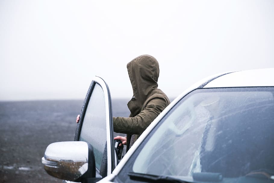 Hiker in a hooded jacket coming out of car with camera to take photographs