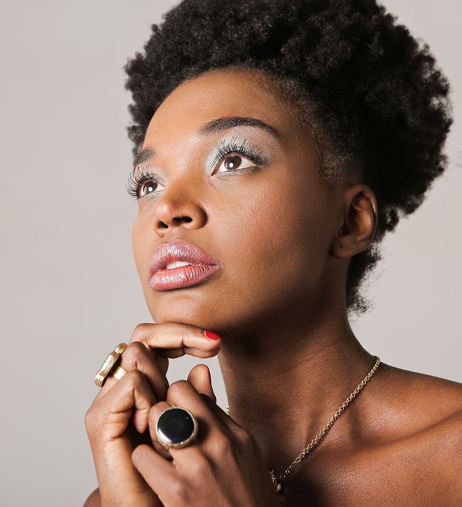 A young African woman wearing jewelry posing indoors with her fingers on her chin