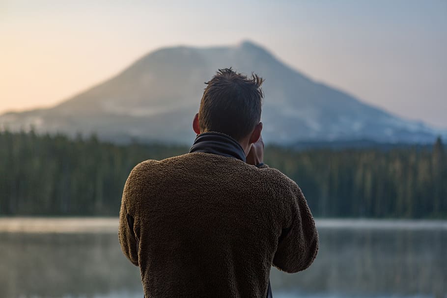 depth of field photography of man in gray sweater standing in front of mountain, HD wallpaper