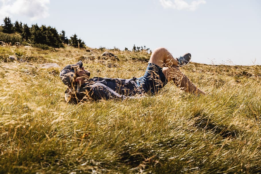 Happy man lying on green grass meadow in mountains enjoying the sun