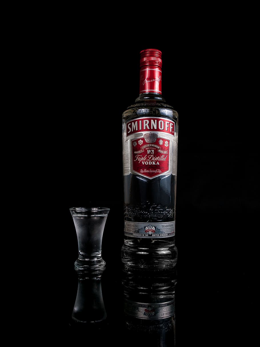 Smirnoff vodka bottle besides shot glass, black background, studio shot