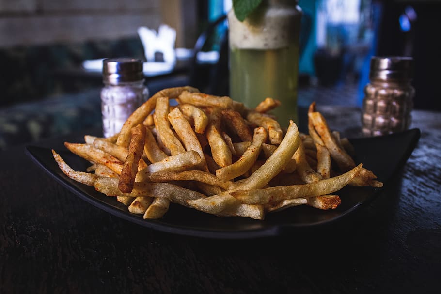 potato fries on black ceramic plate on top of wooden table, food