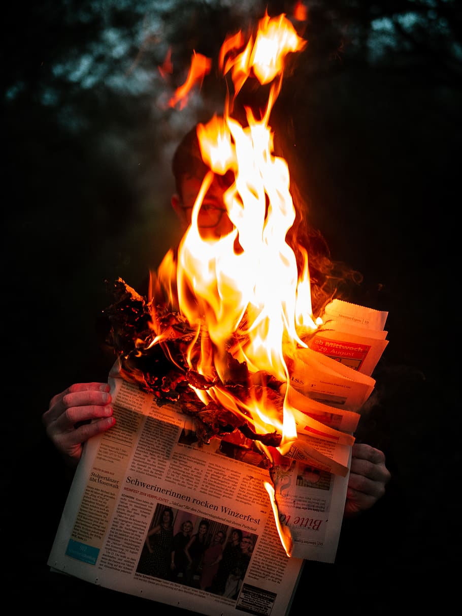 person holding burning newspaper, fire, flame, bonfire, text