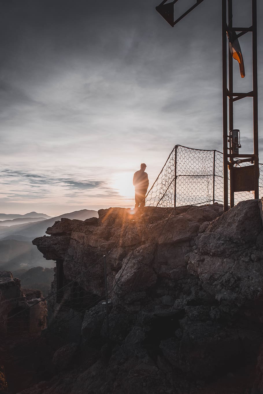 silhouette of man standing on cliff near metal fence, chair, furniture