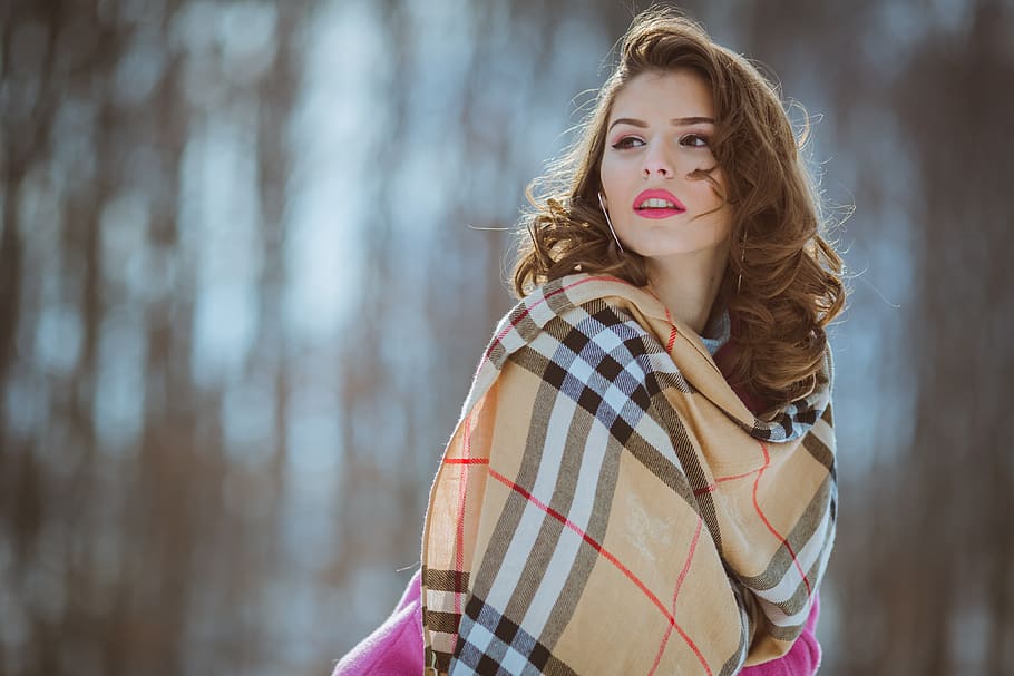 woman with brown, black, red, and white Burberry scarf standing near trees shallow focus photography during daytime