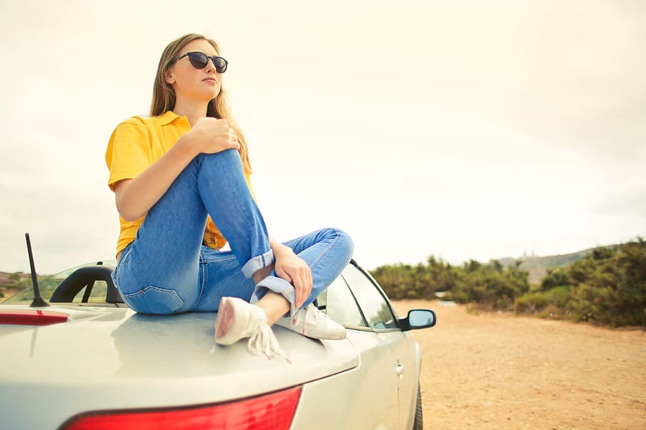 Young Woman Wearing Half-Sleeved Yellow Shirt and Denim Jeans With Black Sunglasses Sitting on Convertible Silver Car