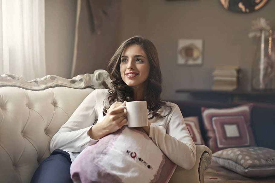 Woman Wearing White Top Drinking Beverage from White Ceramic Mug While Lying on Sofa Inside Well Lit Room HD wallpaper